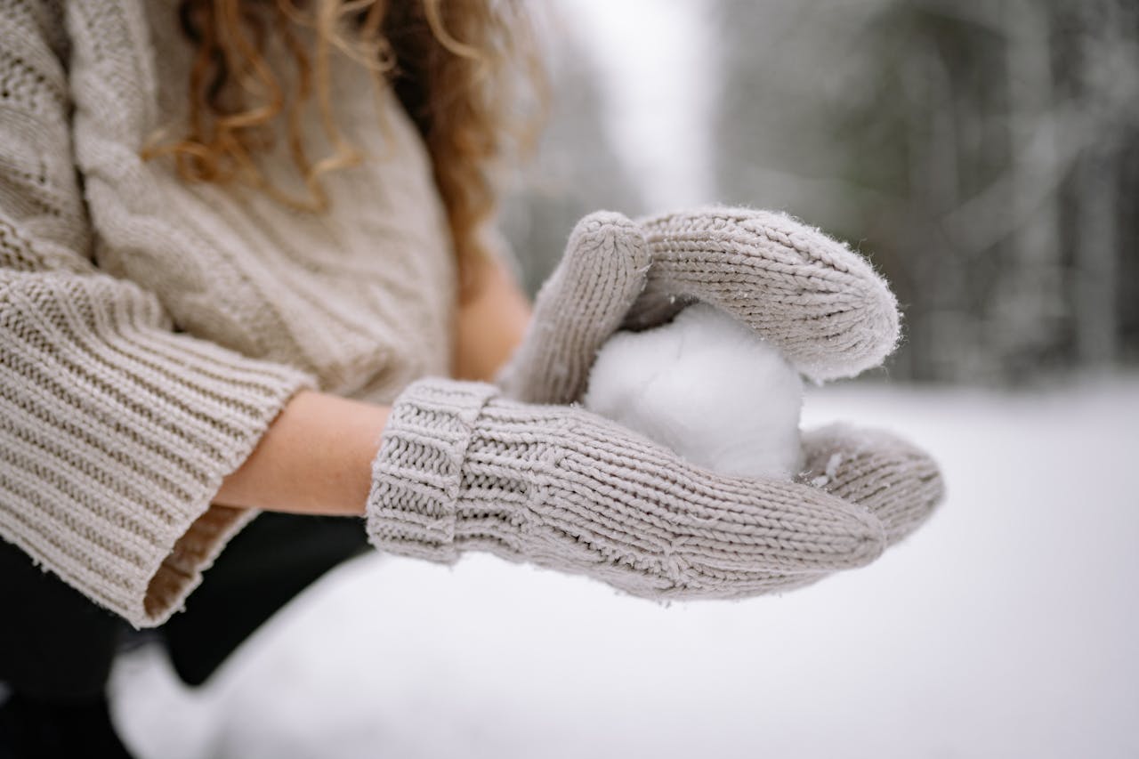 Close-up of knitted gloves holding a snowball, capturing the essence of winter fun.